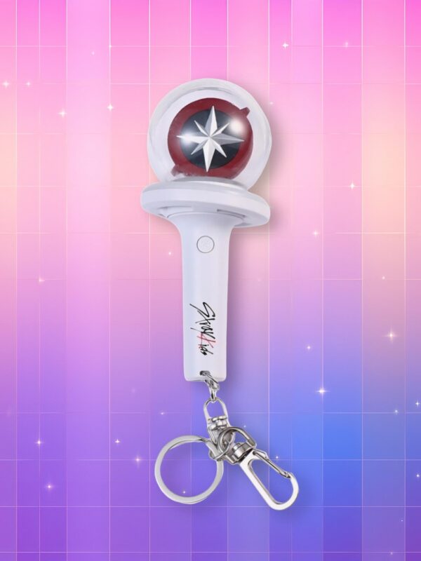 Un lightstick Stray Kids version porte-clés présentant un manche blanc et un bulbe translucide contenant un cercle rouge et noir avec une rosace des vents blanche en son centre, sur un fond artificiel coloré avec un gradient allant du rose au violet.
