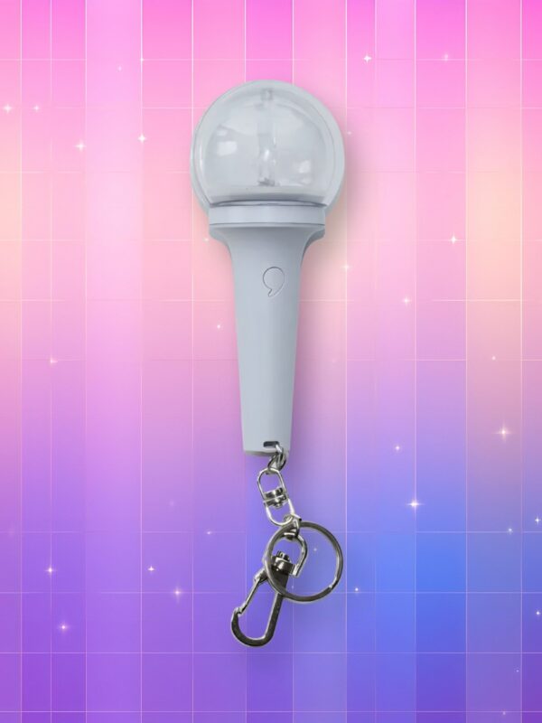 Un lightstick Ive version porte-clés entièrement blanc, présentant un manche légèrement en entonnoir et un bulbe transparent enfermant le logo du group, sur un fond artificiel coloré avec un gradient allant du rose au violet.