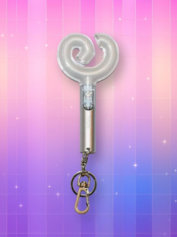 Un Aespa lightstick version porte-clés 2 de couleur argentée avec un bulbe légèrement translucide en forme de bretzel représentant le logo du groupe, sur un fond artificiel coloré avec un gradient allant du rose au violet.