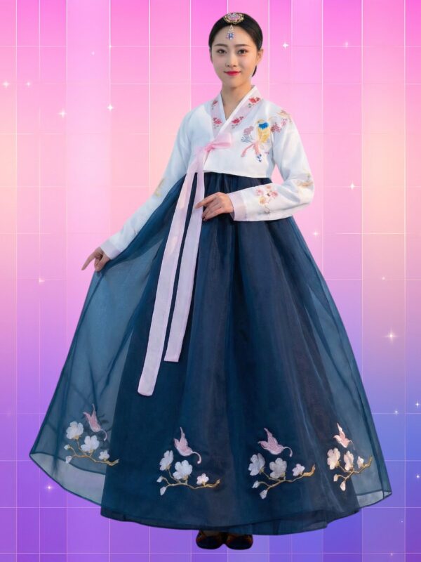 Une femme asiatique portant un hanbok traditionnel avec un jeogori blanc brodé de fleurs et d’un oiseau, un otgoreum rose noué au centre et une chima bleu marine ample ornée de broderies florales, sur un fond rose-violet.