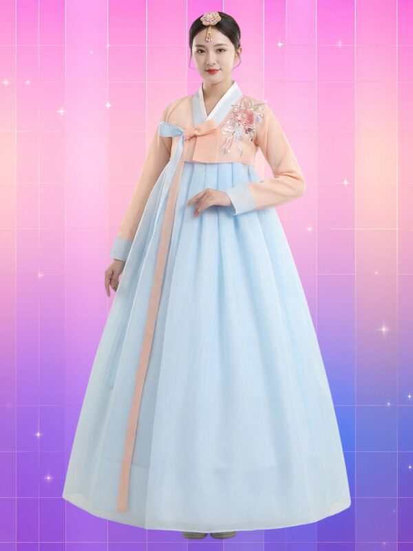 Femme coréenne en hanbok moderne avec un jeogori pastel pêche brodé de fleurs, un otgoreum bicolore bleu et rose, et une chima bleu ciel fluide et ample, sur fond rose-violet lumineux.