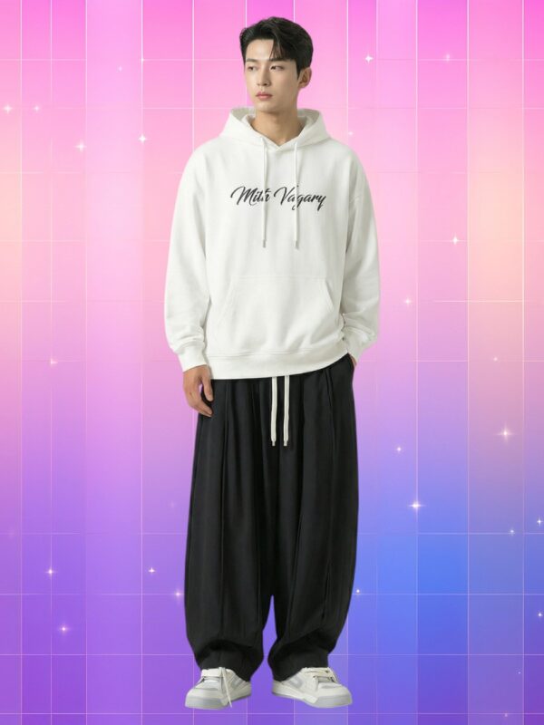Homme asiatique portant un pantalon coréen coupe large style icône moderne, noir fluide à cordon blanc, avec hoodie blanc imprimé, debout sur fond rose-violet lumineux.