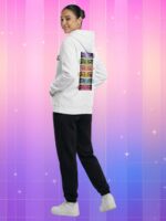 Une jeune femme souriante porte le pull blanc KATSEYE fan K-pop aux yeux emblématiques, dos tourné, huit regards colorés imprimés dans le dos sur fond rose-violet.