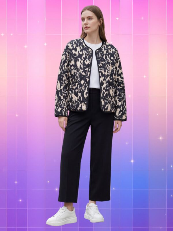 Femme portant une veste kimono femme graphique matelassée moderne noire et beige, coupe droite avec poches, sur fond dégradé rose et violet.