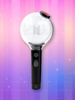 Un lightstick BTS Edition spéciale avec un manche noir comprenant deux boutons et un bulbe transparent avec inscrit "BTS" dessus ainsi que le logo du groupe, sur un fond artificiel coloré avec un gradient allant du rose au violet.