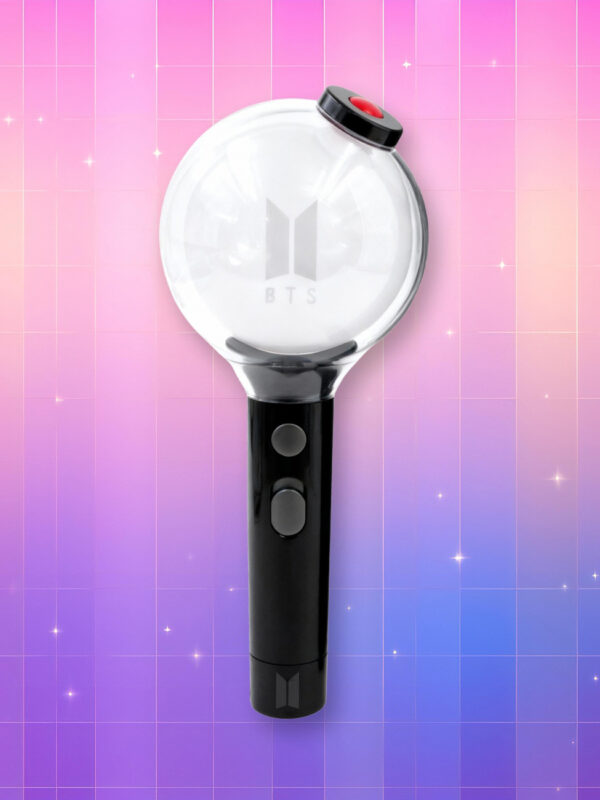Un lightstick BTS Edition spéciale avec un manche noir comprenant deux boutons et un bulbe transparent avec inscrit "BTS" dessus ainsi que le logo du groupe, sur un fond artificiel coloré avec un gradient allant du rose au violet.