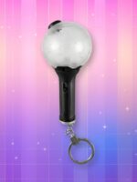 Un lightstick BTS version porte-clé avec un manche noir, un bulbe transparent et une chaîne porte-clé au bout, sur un fond artificiel coloré avec un gradient allant du rose au violet.