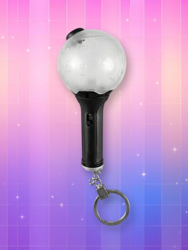 Un lightstick BTS version porte-clé avec un manche noir, un bulbe transparent et une chaîne porte-clé au bout, sur un fond artificiel coloré avec un gradient allant du rose au violet.