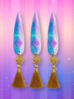 Des jouets Kpop Demon Hunters couteaux de Zoey, avec des lames en résines et pompoms dorés, sur un fond artificiel coloré avec un gradient allant du rose au violet.