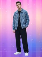 Homme portant une veste style coréen homme denim à carreaux bleus sur tee-shirt noir, avec pantalon large et baskets blanches, devant un fond rose-violet vibrant.