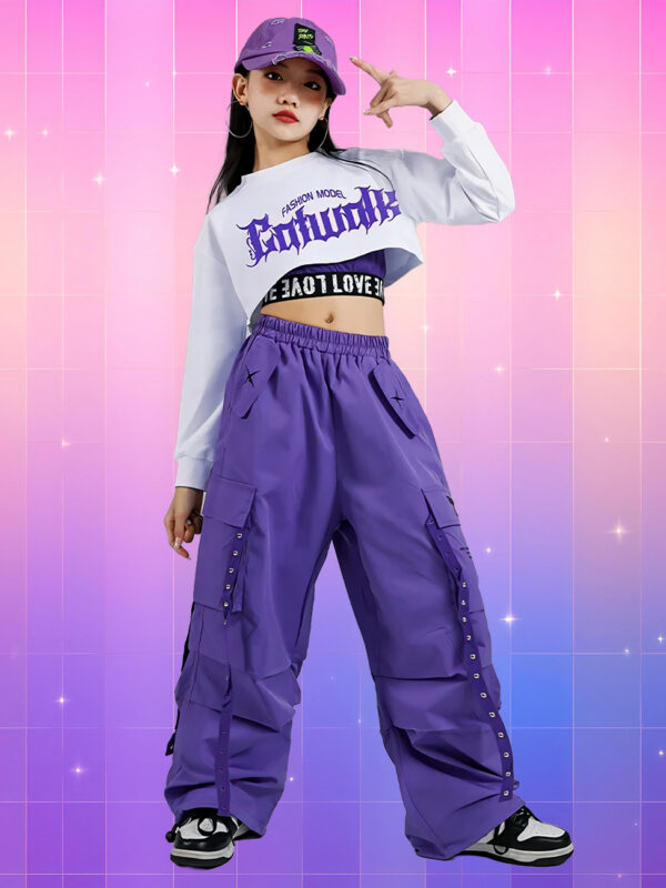 Une jeune fille portant une tenue kpop enfant streetwear 3 pièces : pantalon cargo violet, crop top blanc et casquette, sur un fond rose et violet.