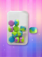 Jeu coréen des pierres Gonggi colorées dans une boite plastique rectangulaire sur fond dégradé de rose à violet.