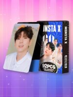Un lot de 92 cartes Lomo Monsta X présenté avec une boîte illustrée du groupe de K-pop et une carte montrant un chanteur souriant en chemise blanche, le tout posé sur un fond dégradé rose et bleu avec un motif de grille étoilée.