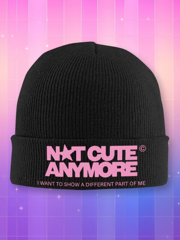 Un bonnet kpop Illit Not Cute Anymore de couleur noire avec une inscription rose, sur un fond dégradé rose et violet parsemé de petites étoiles étincelantes.