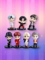 Un lot de 7 figurines kpop BTS représentant les membres du groupe avec des styles et couleurs de cheveux variés, posés sur des socles noirs devant un fond quadrillé aux reflets roses et violets.