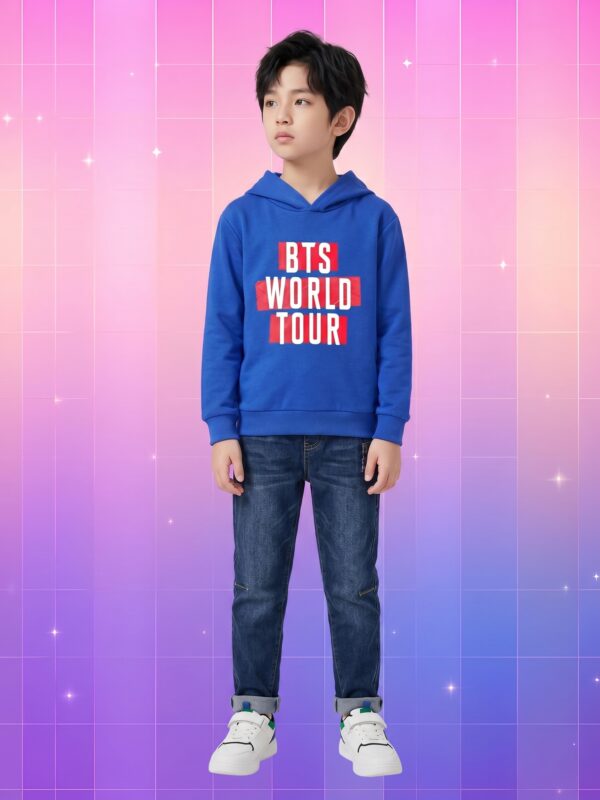 Un petit garçon asiatique portant un pull kpop enfant BTS tournée mondiale bleu et rouge sur un fond coloré rose et violet.