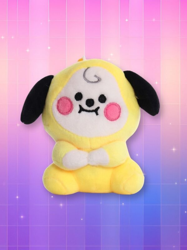 Une peluche Kpop BTS BT21 Chimmy jaune avec de grandes oreilles noires, un visage rond souriant et des joues roses, posée sur un fond dégradé rose et violet.