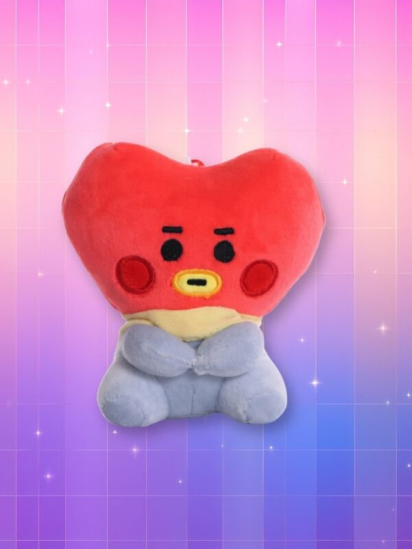Une peluche Kpop BTS BT21 Tata en forme de cœur rouge, avec un petit visage noir et un corps gris, posée sur un fond rose et violet brillant.