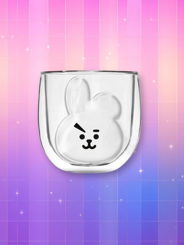 Un mug Kpop transparent BTS BT21 Cooky en verre, avec le visage de Cooky imprimé en noir, posé sur un fond rose et violet scintillant.