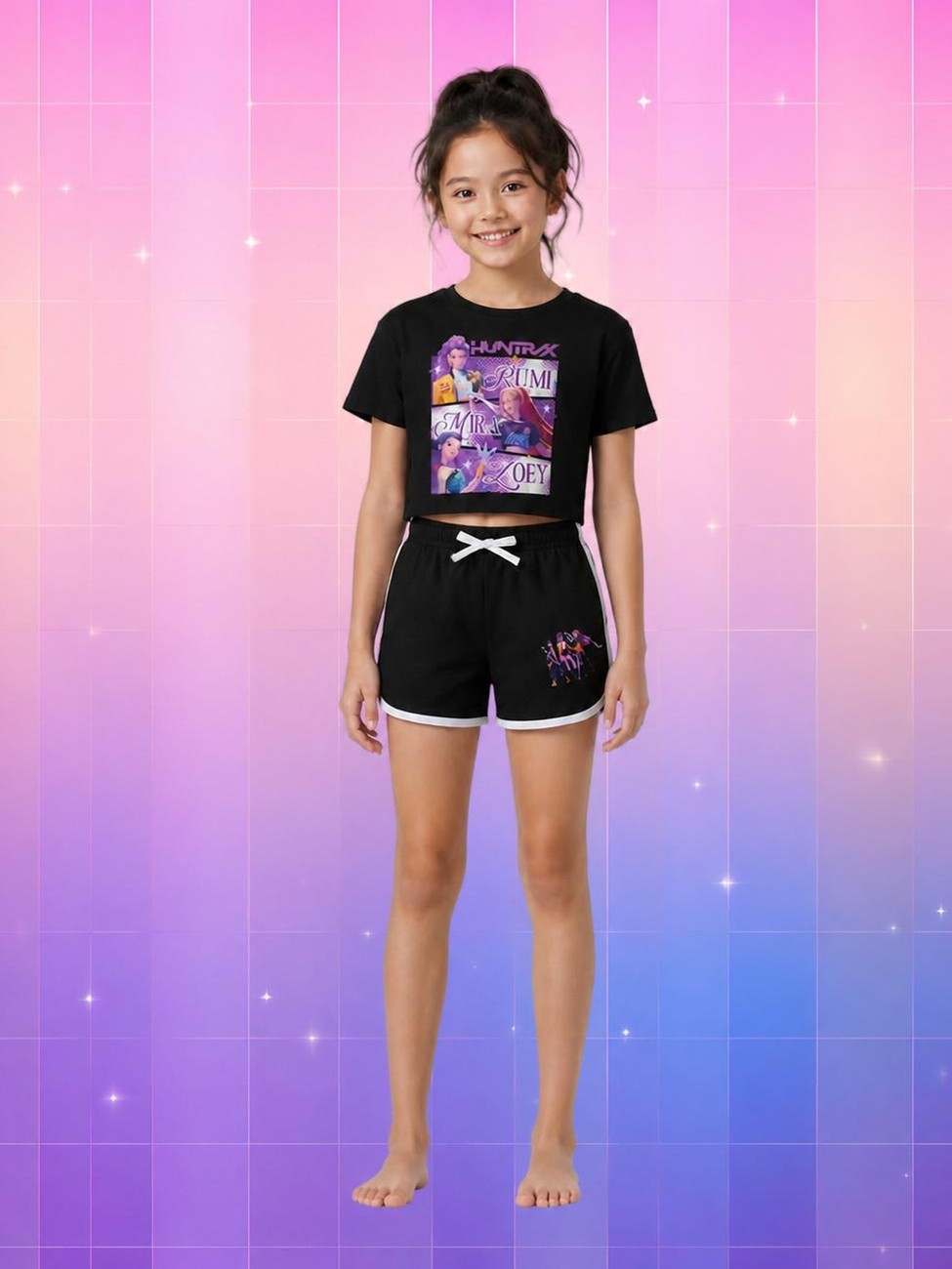 Une jeune fille souriante porte le pyjama Kop Demon Hunters Huntrix d'été noir, avec un haut court et un short assorti, devant un fond rose et violet lumineux.