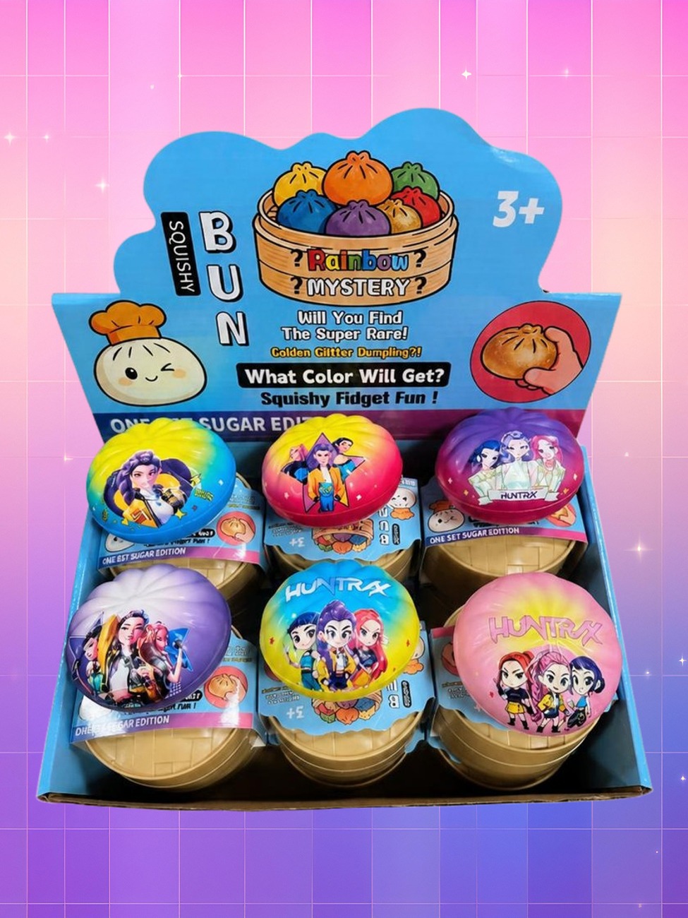 Une boîte ouverte présente plusieurs jouets colorés Jouet squishy Kpop Demon Hunters en blind box surprise, décorés de personnages, sur un fond rose et violet.