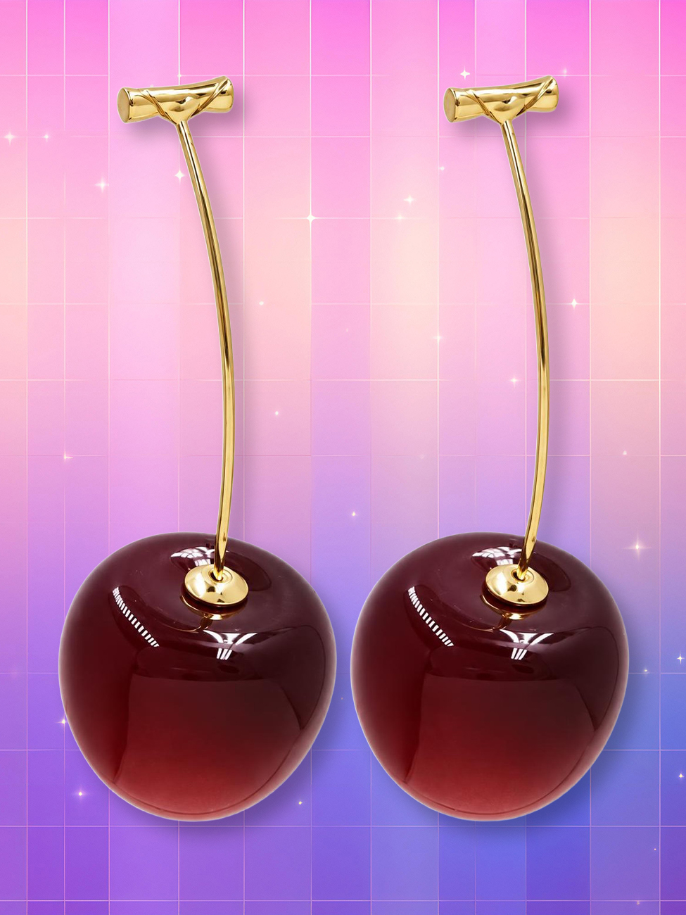 Des boucles d'oreille tendance en forme de cerise rouges et brillantes, suspendues à de longues tiges dorées sur un fond rose et violet scintillant.