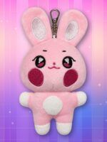 Une peluche porte-clés DDEONGbyeoli ANITEEZ rose, avec de grandes oreilles, des joues rouges et un crochet métallique, posée sur un fond dégradé rose et violet.
